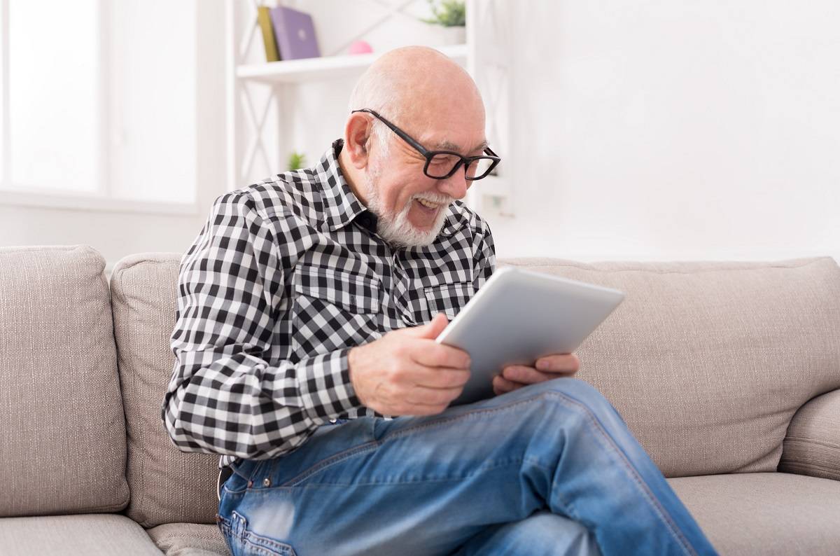 happy senior man sitting on a couch and reading news on his tablet